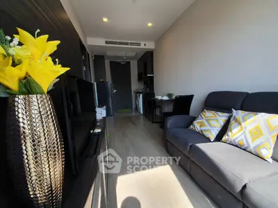 Modern living room with stylish decor and open kitchen layout, featuring a cozy sofa and vibrant yellow accents.