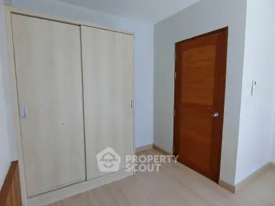 Spacious bedroom with wooden wardrobe and door, perfect for modern living.