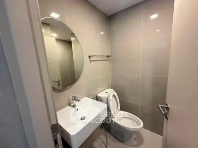 Modern bathroom with sleek fixtures and neutral tiles, featuring a round mirror and contemporary design.