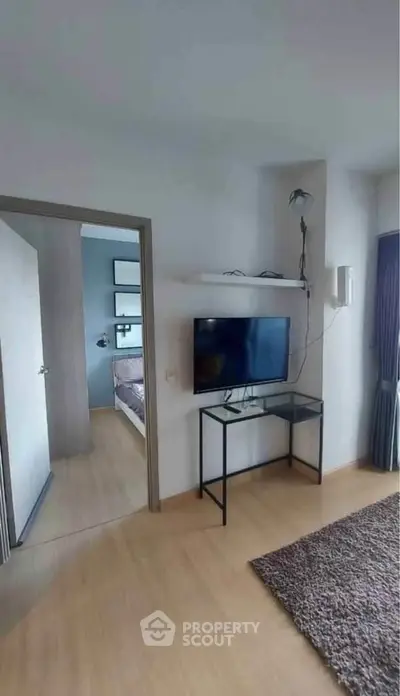 Modern living room with wall-mounted TV and glass table, leading to a cozy bedroom.