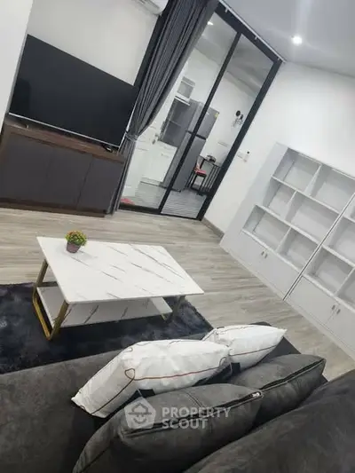 Modern living room with sleek furniture and large TV, featuring a stylish coffee table and elegant decor.