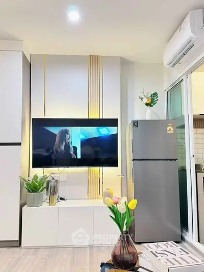 Modern living room with sleek TV setup and stylish decor, featuring a stainless steel fridge and vibrant flowers.