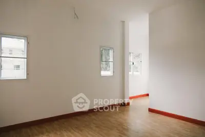 Spacious empty room with wooden flooring and natural light from multiple windows.