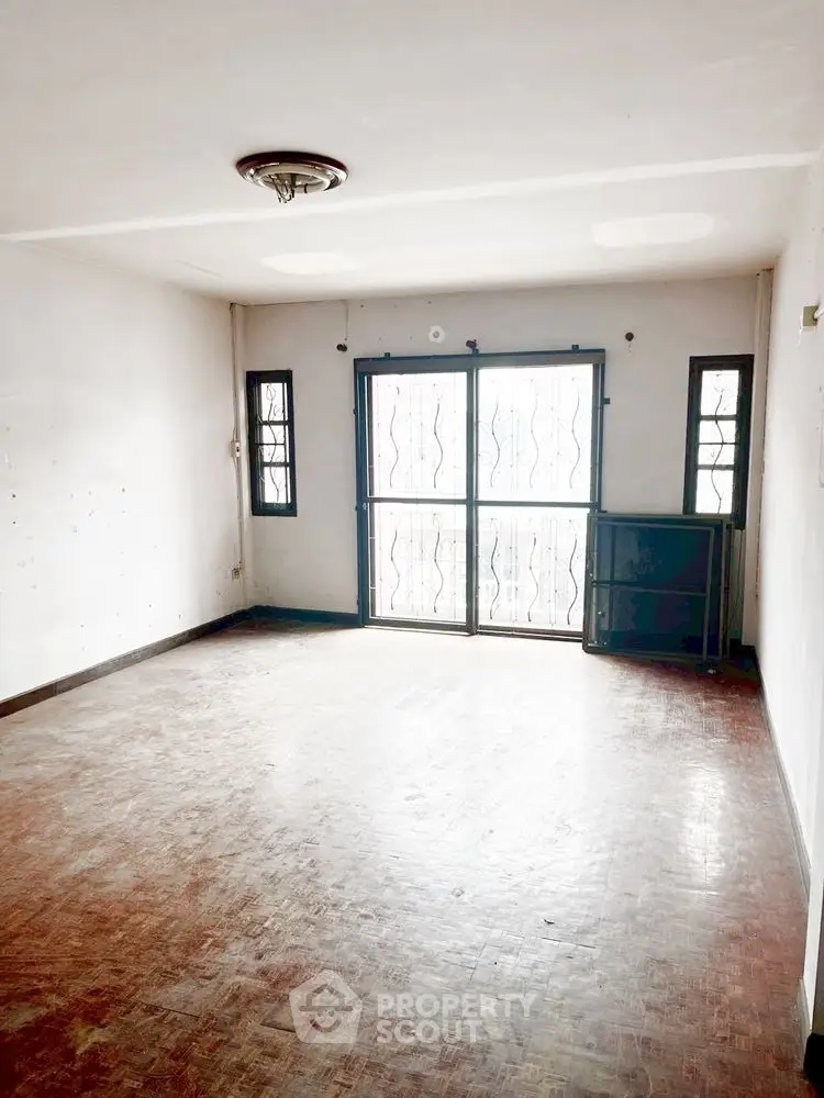 Spacious empty living room with parquet flooring and large windows for natural light.