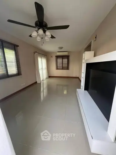 Spacious living room with modern ceiling fan and large windows for natural light.