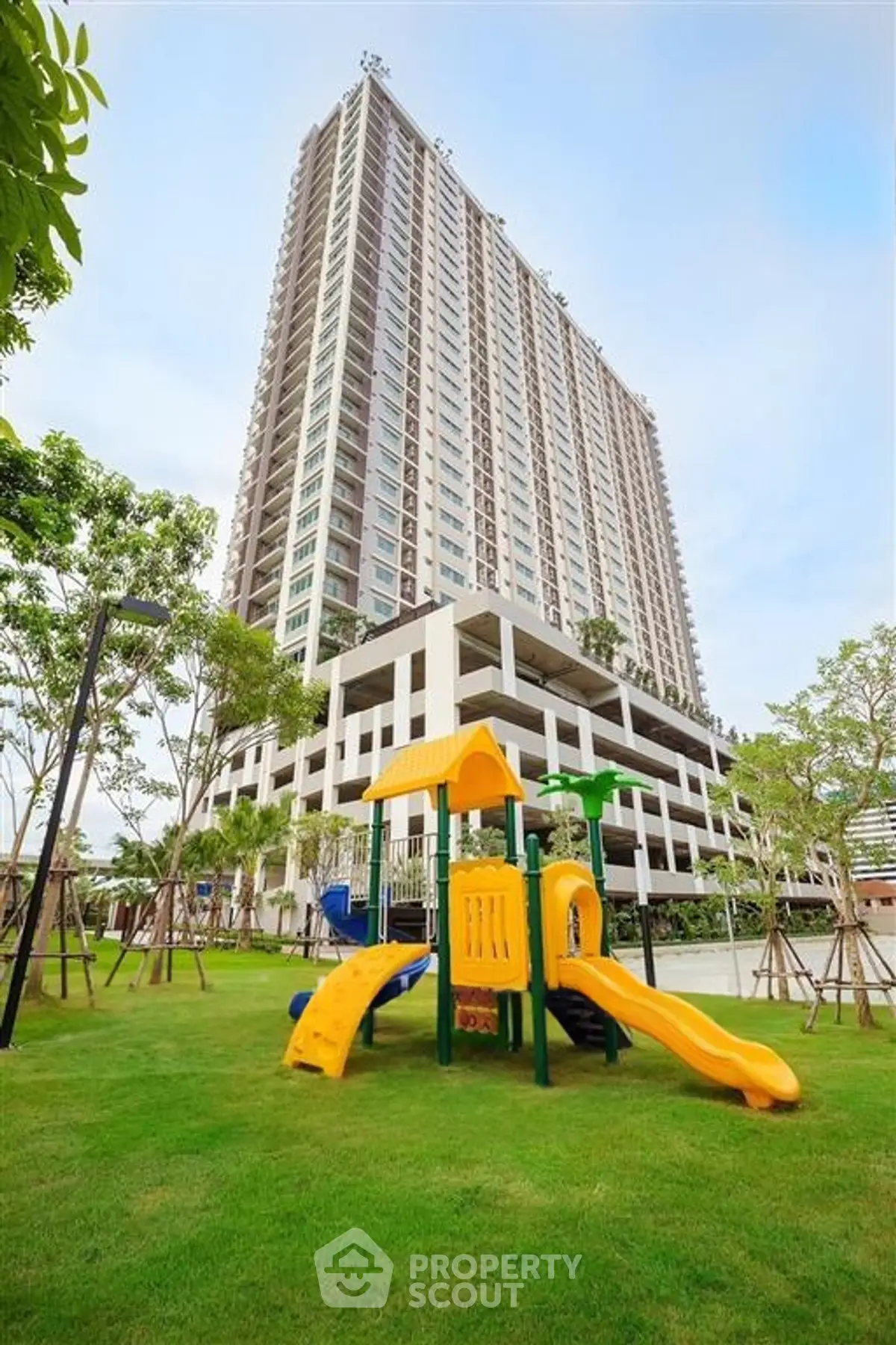 Modern high-rise building with lush green playground area, perfect for families seeking urban living with outdoor amenities.