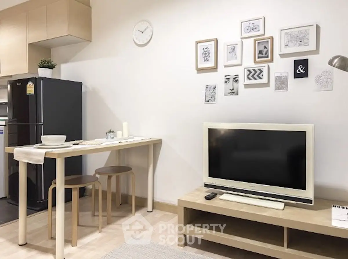 Modern living room with stylish decor and compact dining area, featuring a sleek black fridge and wall art.