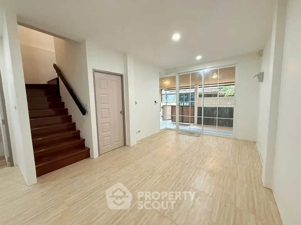 Spacious living room with wooden staircase and large windows leading to a balcony.