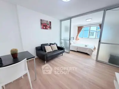Modern open-layout apartment with cozy living area and bright bedroom separated by glass doors.