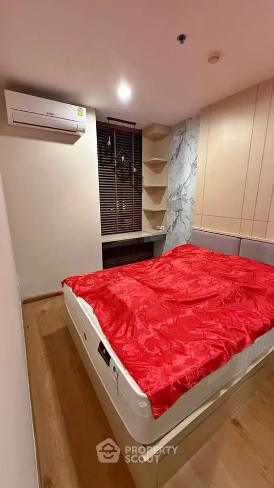 Cozy bedroom with modern design, featuring a red bedspread, air conditioning, and stylish shelving.