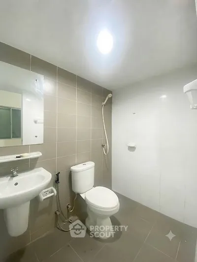 Modern bathroom with sleek fixtures and neutral tiles, featuring a shower and toilet.
