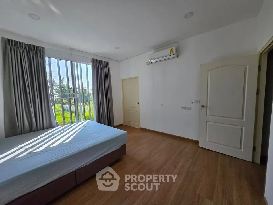 Spacious bedroom with large window and wooden flooring, featuring modern air conditioning unit.