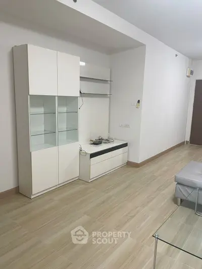 Modern minimalist living room with sleek white cabinetry and light wood flooring.