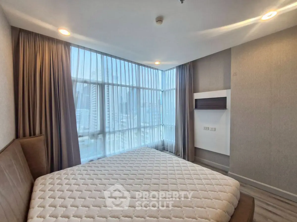 Modern bedroom with large windows and city view, featuring elegant curtains and minimalist design.