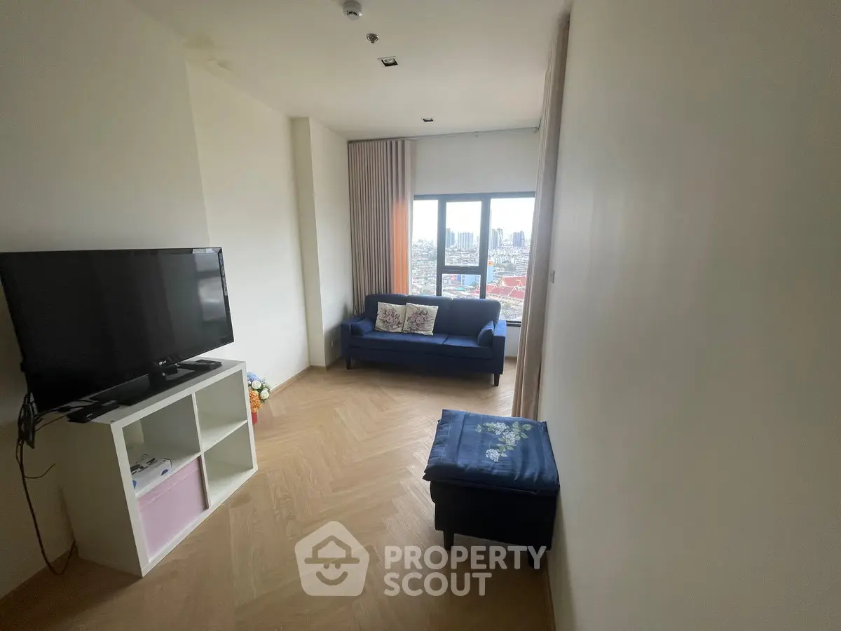 Bright living room with city view, featuring a cozy sofa and modern TV setup.