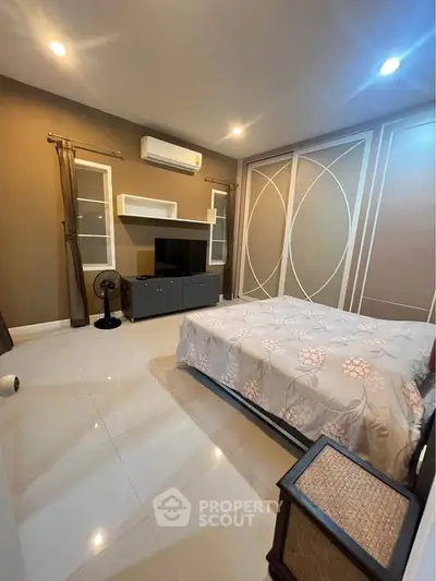 Spacious bedroom with modern decor and ample natural light, featuring a sleek TV unit and stylish furnishings.