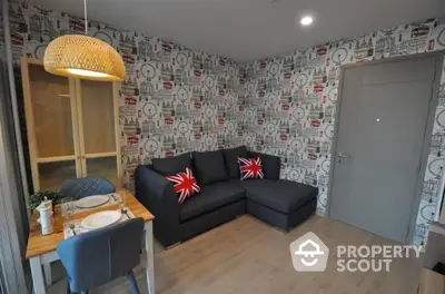 Cozy modern living room with stylish wallpaper and comfortable L-shaped sofa adorned with Union Jack cushions, complemented by a quaint dining area.