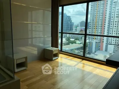 Spacious room with large window offering stunning city view and wooden flooring.