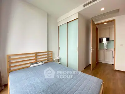 Modern bedroom with wooden bed frame and sliding closet doors, adjacent to a compact kitchen area.