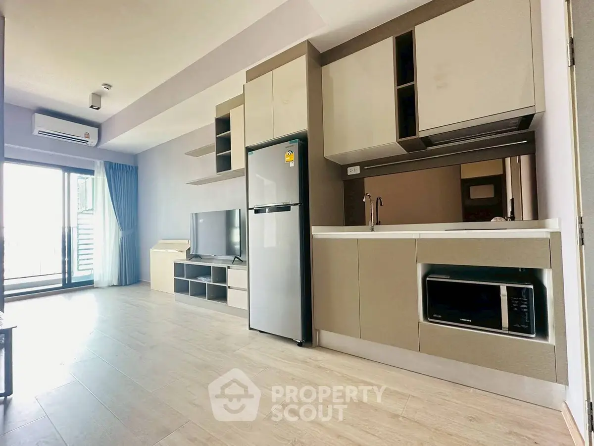 Modern open-plan living room with sleek kitchen and balcony access, featuring contemporary appliances and stylish decor.