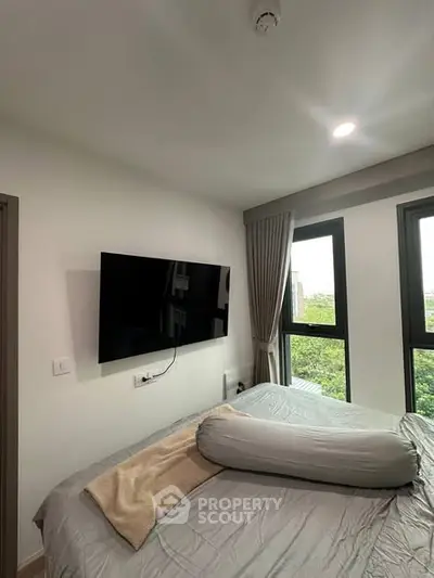 Modern bedroom with large windows and wall-mounted TV, offering a serene view.