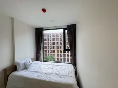 Bright bedroom with large window offering city view and cozy bed setup.