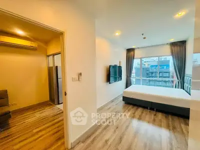 Spacious bedroom with modern decor and large window offering city view, featuring wooden flooring and wall-mounted TV.