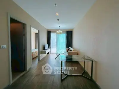 Spacious modern living room with glass table and cozy sofa, leading to a bright bedroom.