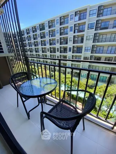 Charming balcony with seating overlooking modern apartment complex and lush greenery.