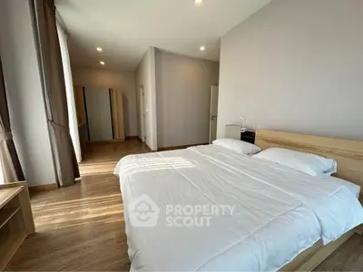 Spacious modern bedroom with wooden flooring and ample natural light