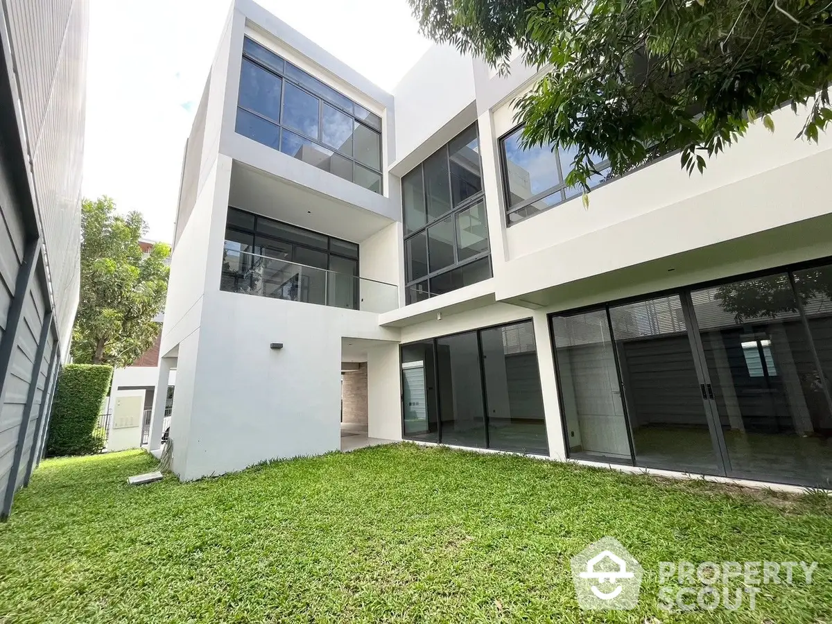 Modern two-story home boasting large windows, a spacious balcony, and a lush green lawn, nestled in a serene neighborhood, perfect for luxurious living.