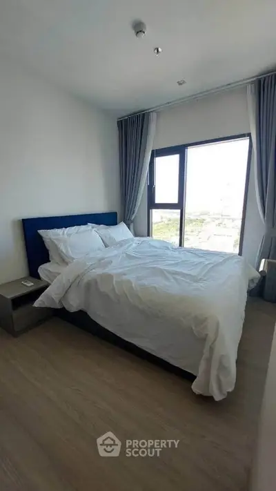Modern bedroom with large window and stylish decor in a high-rise apartment.