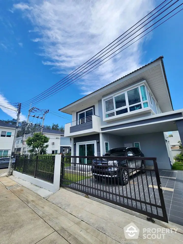 Modern two-story house with carport and lush green lawn under clear blue sky