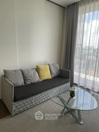 Modern living room with stylish sofa and glass coffee table, featuring floor-to-ceiling windows.