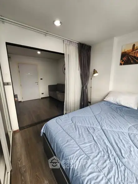 Modern bedroom with blue bedding and view into cozy living area, featuring stylish decor and natural light.