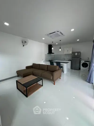 Modern open-plan living room with sleek kitchen and cozy sofa, featuring bright tiles and contemporary appliances.