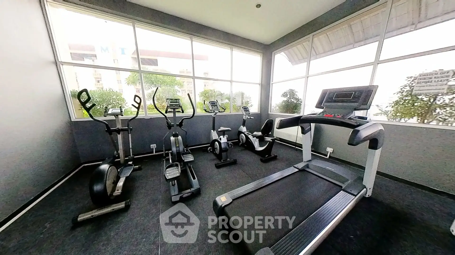 Modern gym with cardio equipment and large windows in a residential building.