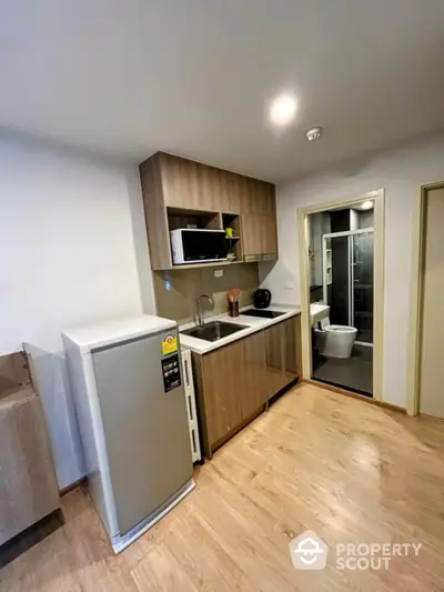 Modern compact kitchen with wooden cabinets and integrated appliances in a cozy apartment.