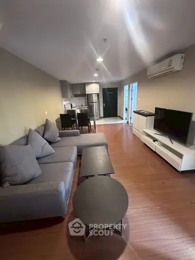 Modern living room with cozy gray sofa, sleek TV setup, and open kitchen layout in stylish apartment.