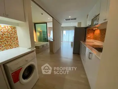 Modern open-plan apartment with stylish kitchen and washing machine, featuring bright interiors and wood flooring.