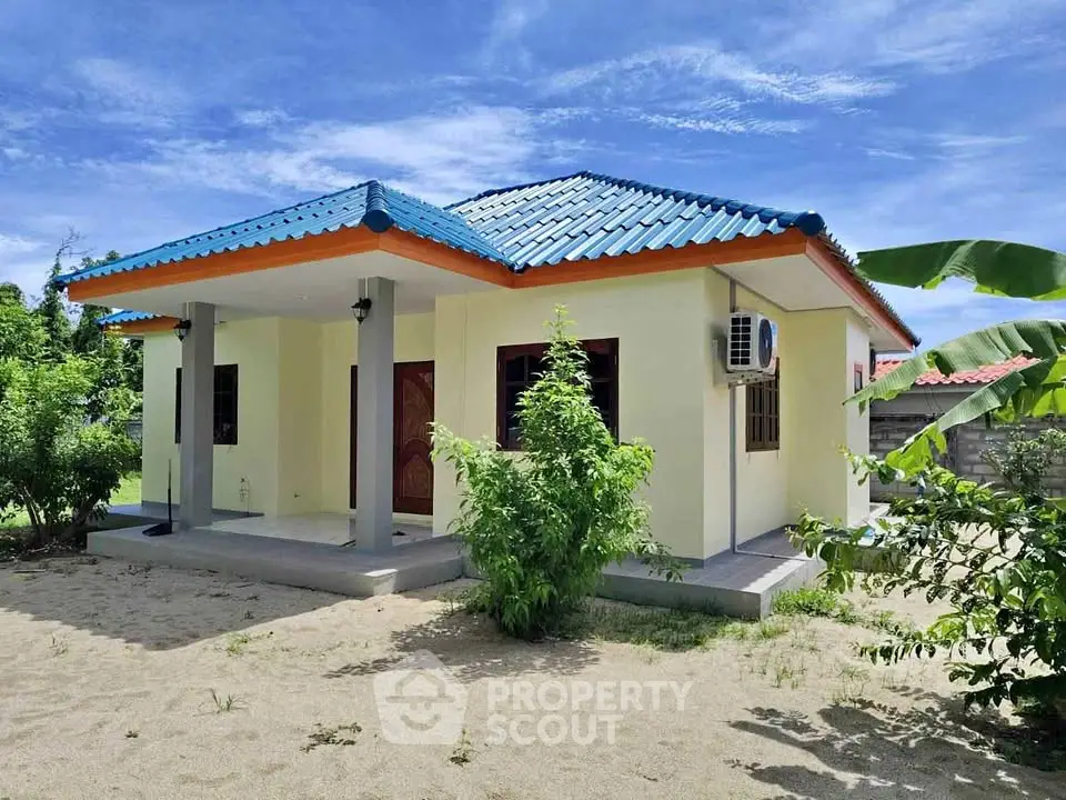 Charming single-story house with vibrant blue roof and lush greenery, perfect for serene living.