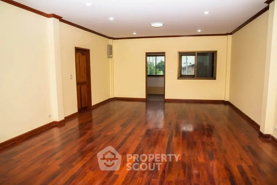 Spacious empty living room with polished wooden floors and large window view.