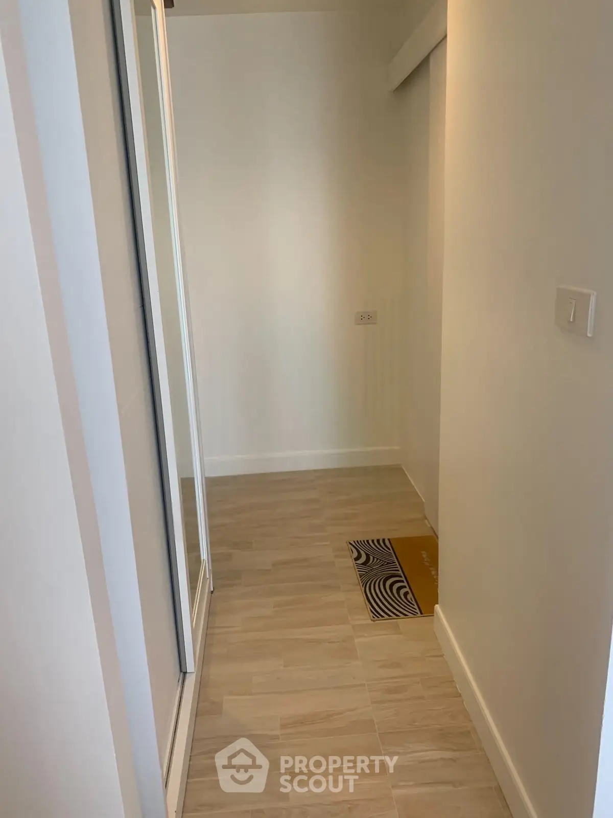 Modern hallway with sleek wooden flooring and mirrored closet doors in a contemporary apartment.