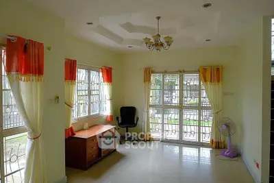 Spacious living room with large windows and elegant curtains, featuring a ceiling chandelier and modern furniture.
