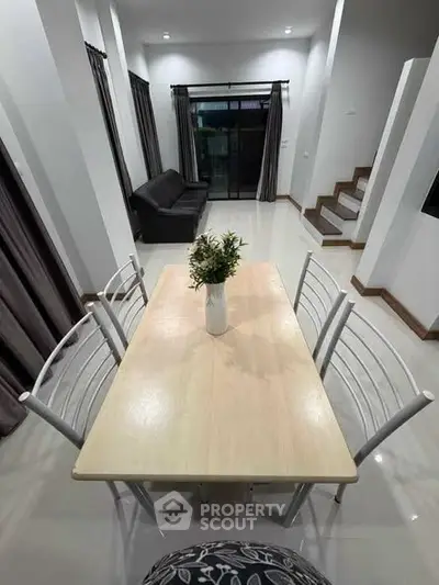 Modern dining area with sleek table and chairs, adjacent to a cozy living room with a sofa and large windows.