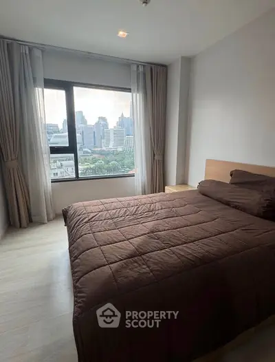 Modern bedroom with city view and large window in high-rise apartment.