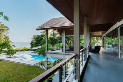 Luxurious villa with spacious balcony overlooking a stunning pool and ocean view, surrounded by lush greenery.
