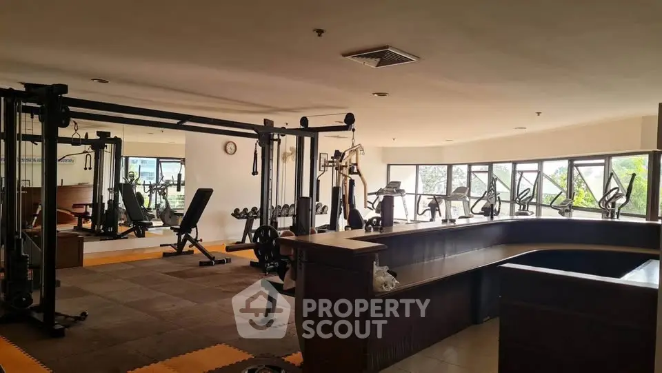 Spacious gym with modern equipment and large windows offering natural light.