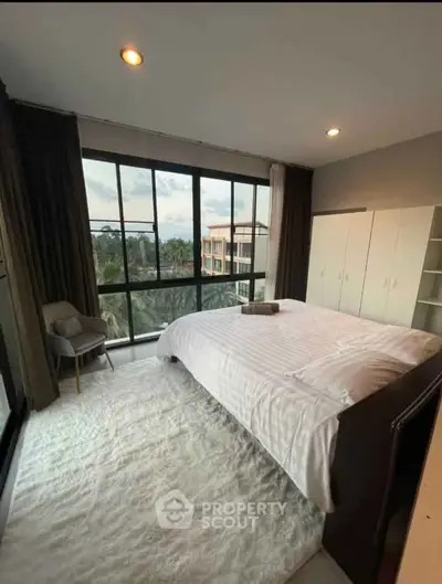 Spacious bedroom with large windows offering a scenic view, modern decor, and ample natural light.