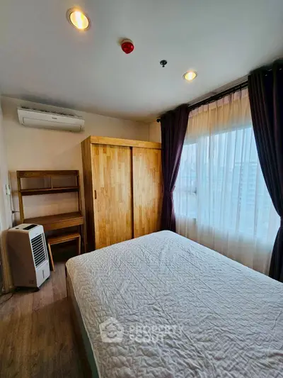 Cozy bedroom with wooden wardrobe and large window offering natural light.